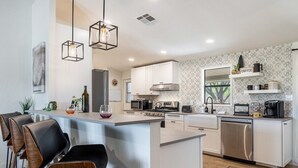 Una cocina moderna con una isla central, taburetes de bar, microondas, estufa y lavavajillas.