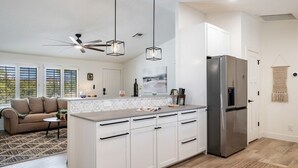 Cocina moderna con armarios blancos, refrigerador de acero inoxidable, luces colgantes y ventilador de techo.