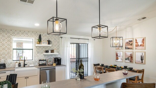 Una cocina moderna con una isla central, luces colgantes y un comedor con sillas y una mesa.