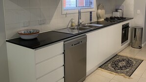 Cozinha moderna com armários brancos, bancada preta, lava-louças, fogão e janela com persianas.