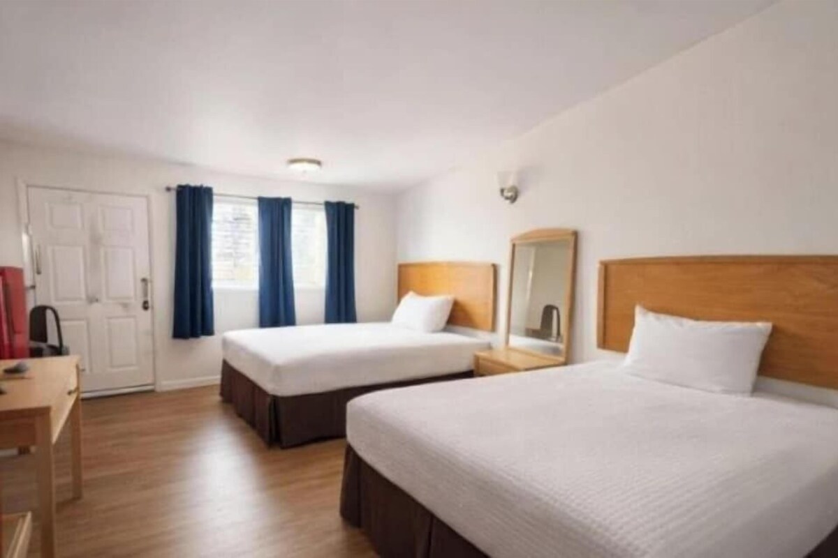 Ein Hotelzimmer mit zwei Betten, einem Schreibtisch, einem Stuhl, einem Kleiderschrank und einem Vorhangfenster.