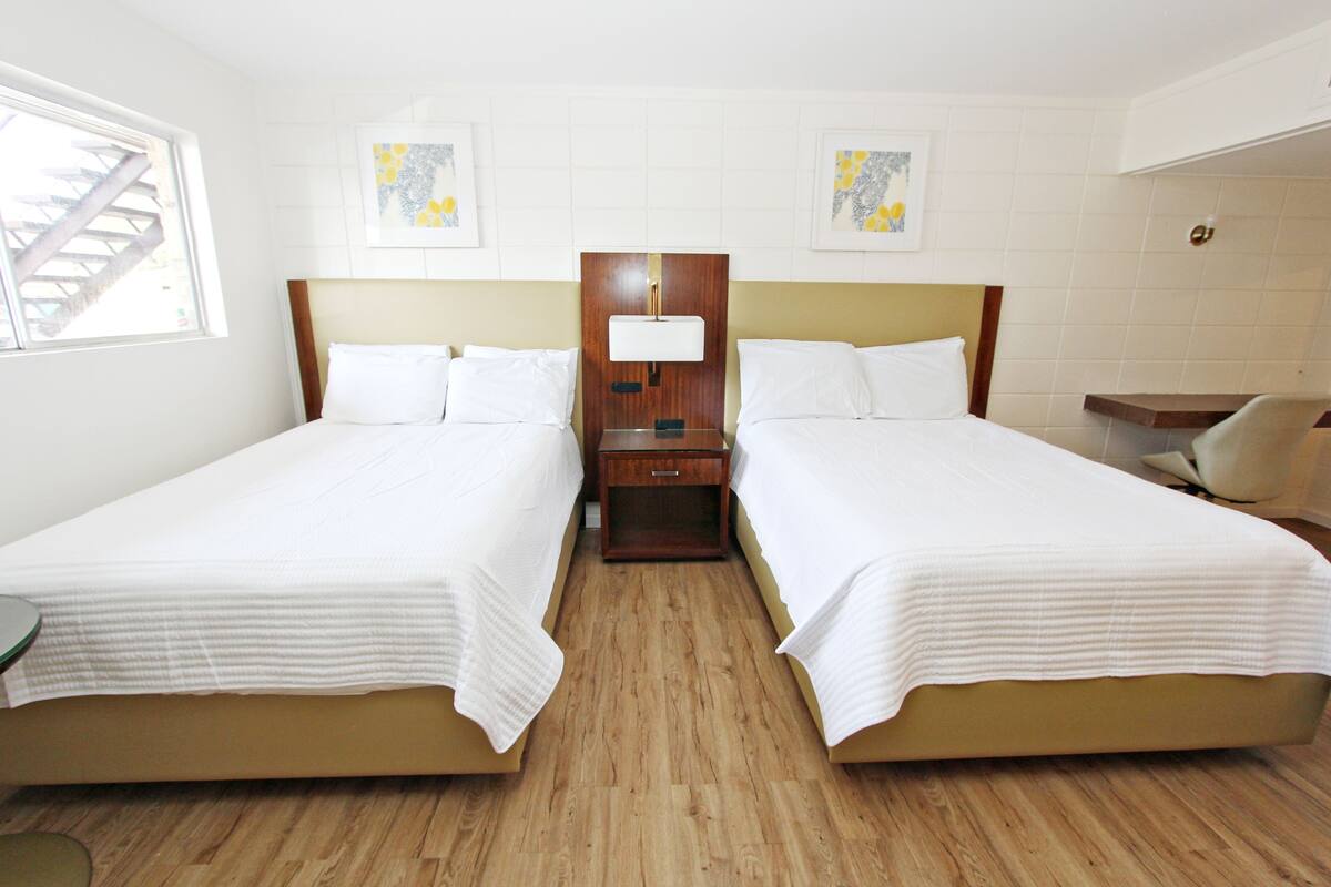 A hotel room with two beds, a nightstand, a lamp, and artwork on the walls.
