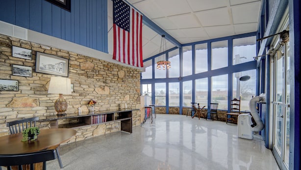 A spacious room with a stone wall, a large American flag, and a view through large windows. - Cannon Inn By Capital O Gonzales Tx (Gonzales)