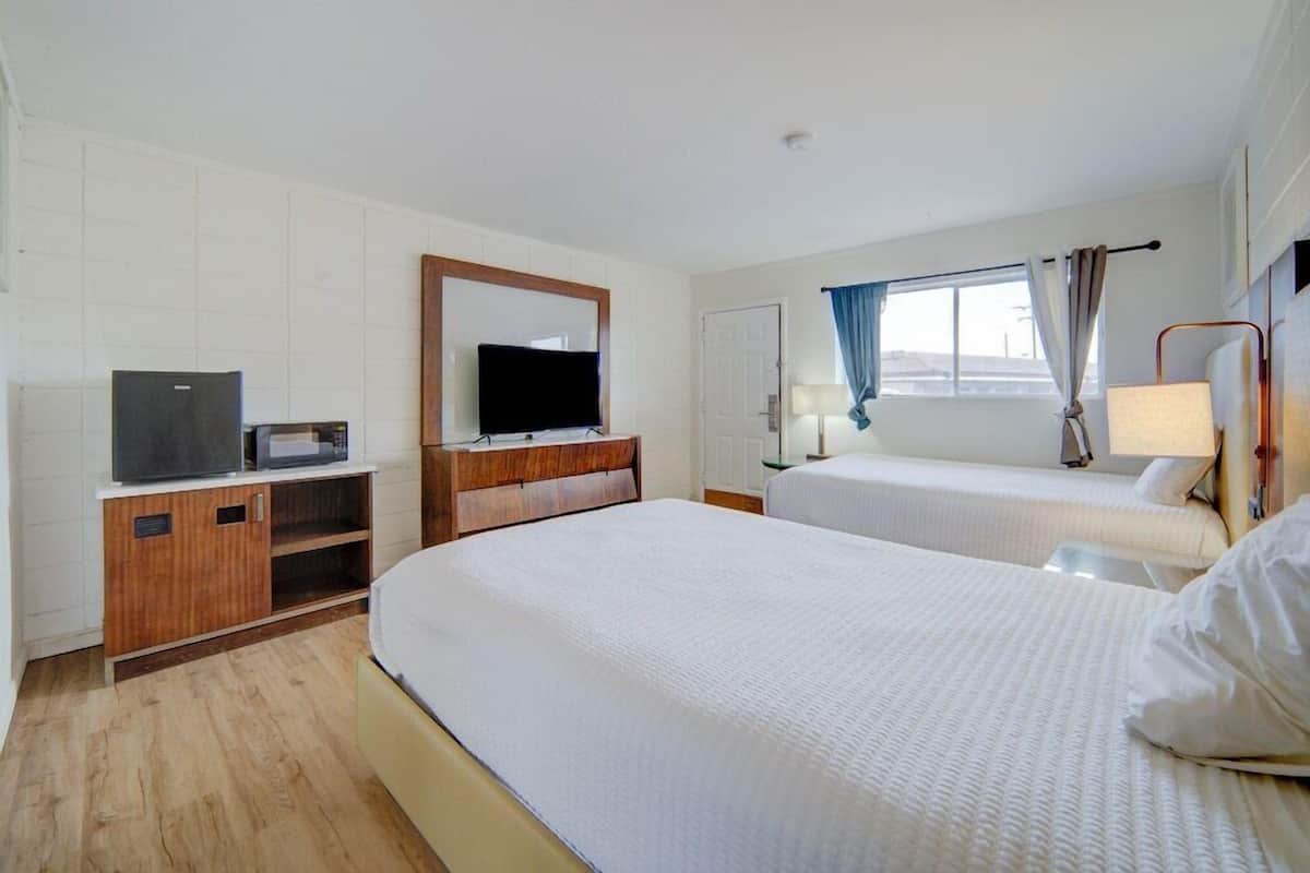 A hotel room with two beds, a television, a desk with a computer, and a window with curtains.