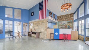A spacious lobby with a large American flag, a stone wall, and a bar area with stools. - Cannon Inn By Capital O Gonzales Tx (Gonzales)