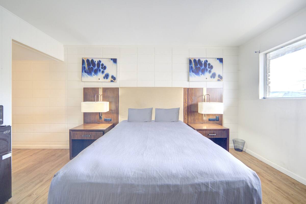 A hotel room with a large bed, two bedside tables with lamps, a small desk, and a window.