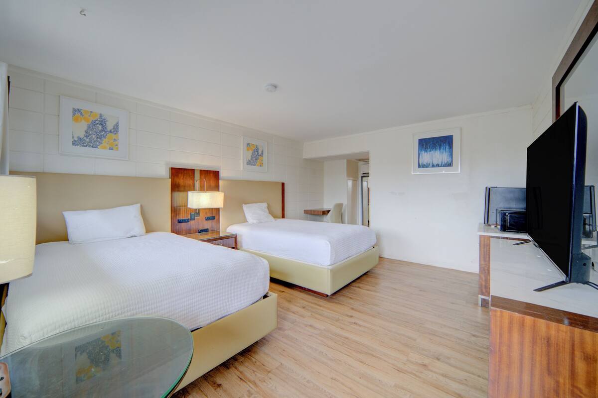 A hotel room with two beds, a TV, and artwork on the walls.