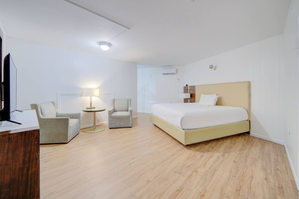 A hotel room with a bed, two armchairs, a desk, a lamp, and a TV.
