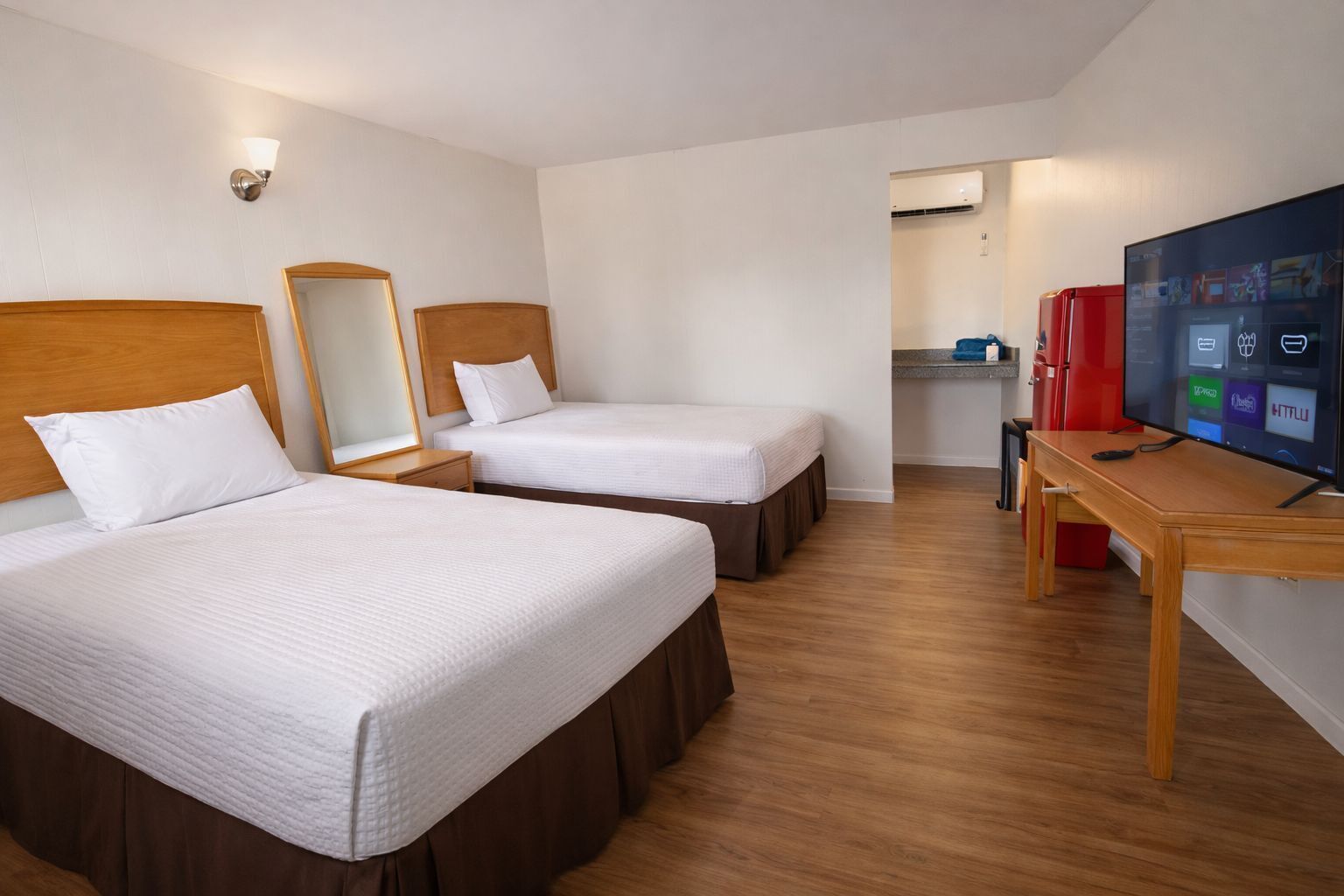 Habitación de hotel con dos camas, televisión, escritorio y espejo.