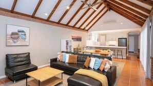 Un'ampia zona giorno con soffitto alto, una cucina sullo sfondo e un'area pranzo.