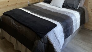 A wooden-paneled room with a bed, a nightstand, a lamp, and a framed picture on the wall.