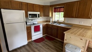 A kitchen with wooden cabinets, a white refrigerator, a microwave, a stove, and a trash bin.