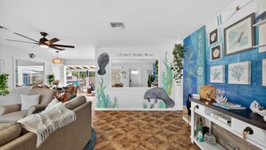 Un salon comprenant un canapé, une table basse, un ventilateur de plafond et un mur orné d’une fresque sur le thème de la mer.