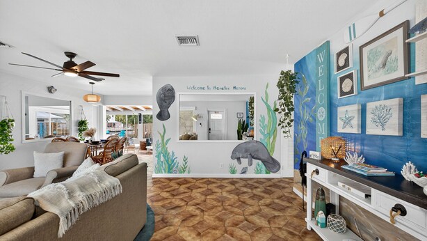 Uma sala de estar com sofá, mesa de centro, ventilador de teto e uma parede com mural de temática marítima.