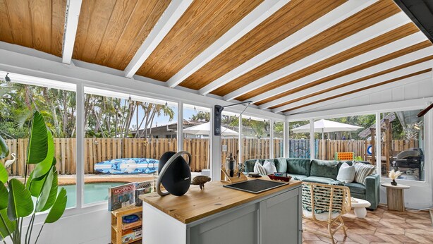 Un vaste espace patio doté d’un plafond en bois, d’une piscine, d’un canapé vert et d’une table à manger.