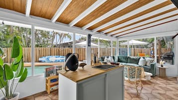 A spacious patio area with a wooden ceiling, a pool, a green sofa, and a dining table.
