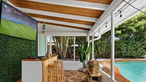 Área externa coberta com piscina, bar de madeira e área de estar.