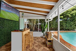 Un espace extérieur abrité comprenant une piscine, un bar en bois et des sièges.