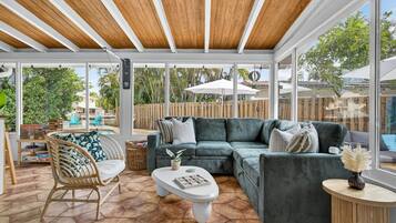 A sunlit patio with a green sectional sofa, a wicker chair, and a white coffee table.