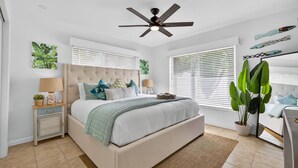 Quarto com cama, mesas de cabeceira, ventilador de teto e janelas amplas com persianas.
