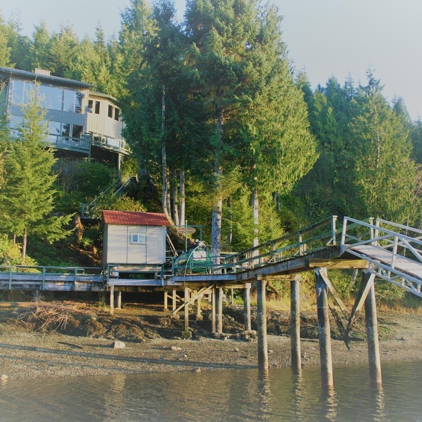 Une jetée en bois s  ’étendant dans une étendue d’eau, avec un petit bâtiment et une plus grande construction dotée d’un toit rouge en arrière-plan.
