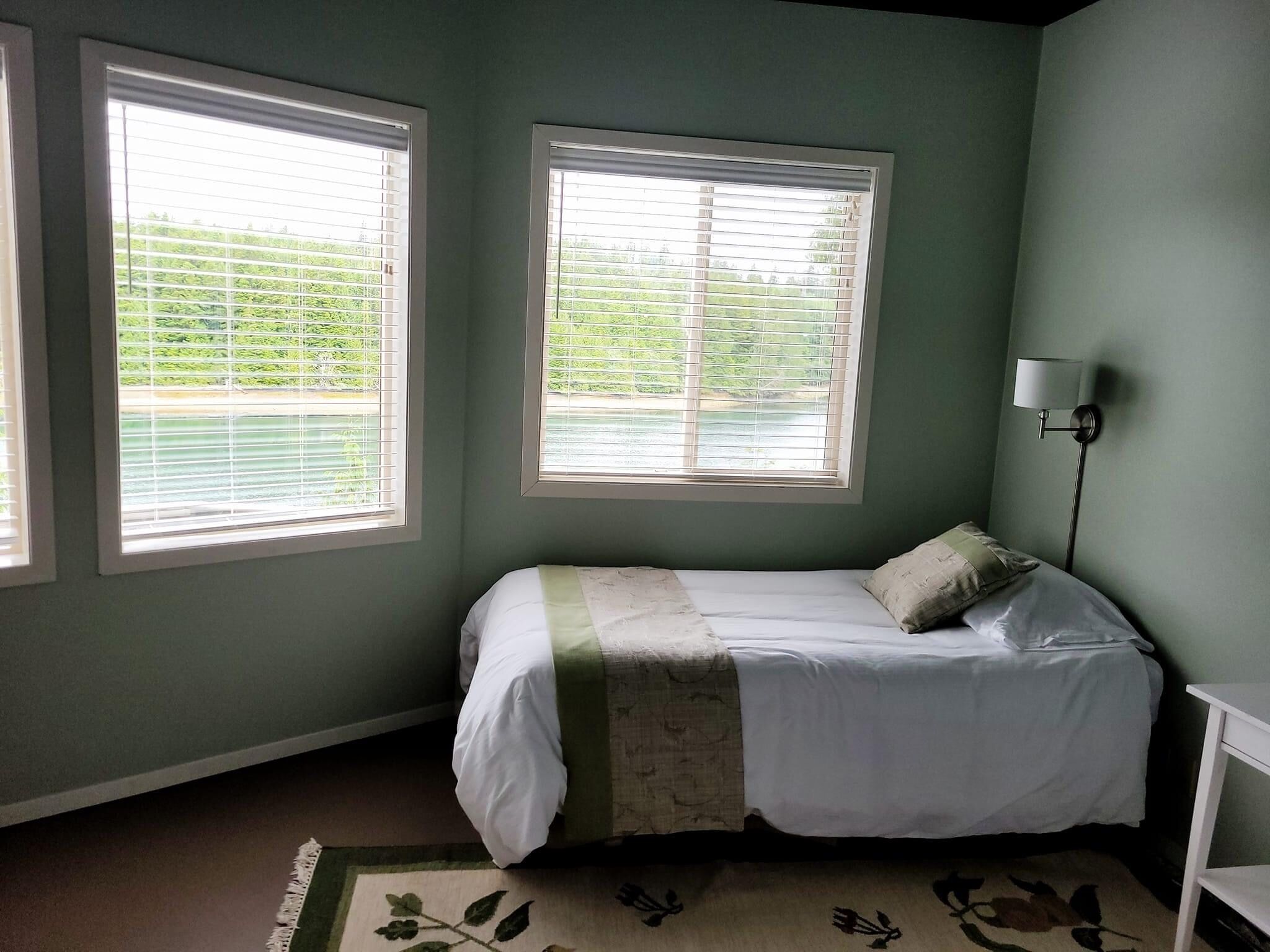 Une chambre à coucher avec un lit, deux fenêtres, une lampe et un tapis.