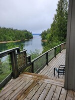 Una terraza de madera con barandilla da vista a un río rodeado de bosque denso.