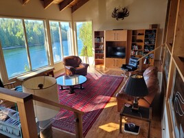 Amplia sala de estar con un gran ventanal con vistas a un lago, un sofá de cuero, una mesa de centro y una estantería.