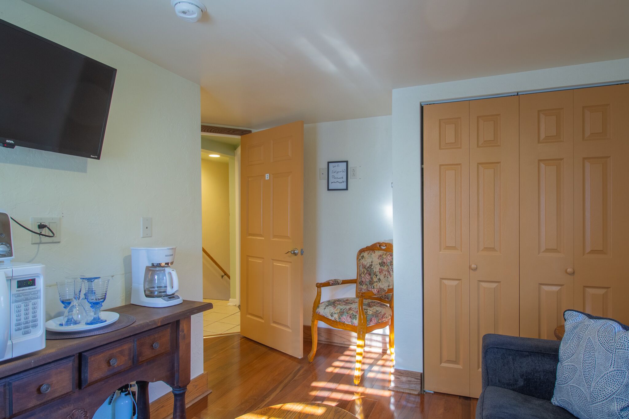 A living room with a flat-screen TV, a coffee maker, and a dining table with glasses.