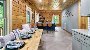 A wooden cabin interior with a dining area, kitchen, and seating. - Modern cabin w/heated pool & hot tub next to pkwy (Sevierville)