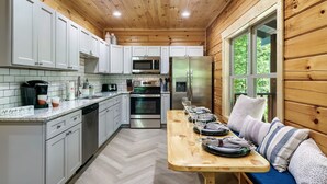 A wooden cabin kitchen with white cabinets, stainless steel appliances, and a dining area with a bench. - Modern cabin w/heated pool & hot tub next to pkwy (Sevierville)