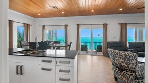 A modern kitchen with a black countertop and white cabinets, a dining area with chairs, and a view of the ocean through large windows. - Ocean Front Property With Pool. - George Town (Exuma)