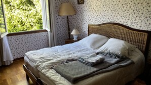 Siististi pedattu sänky, jossa on kuviollinen peitto, yöpöytävalaisin ja kukkakuviotapetti.