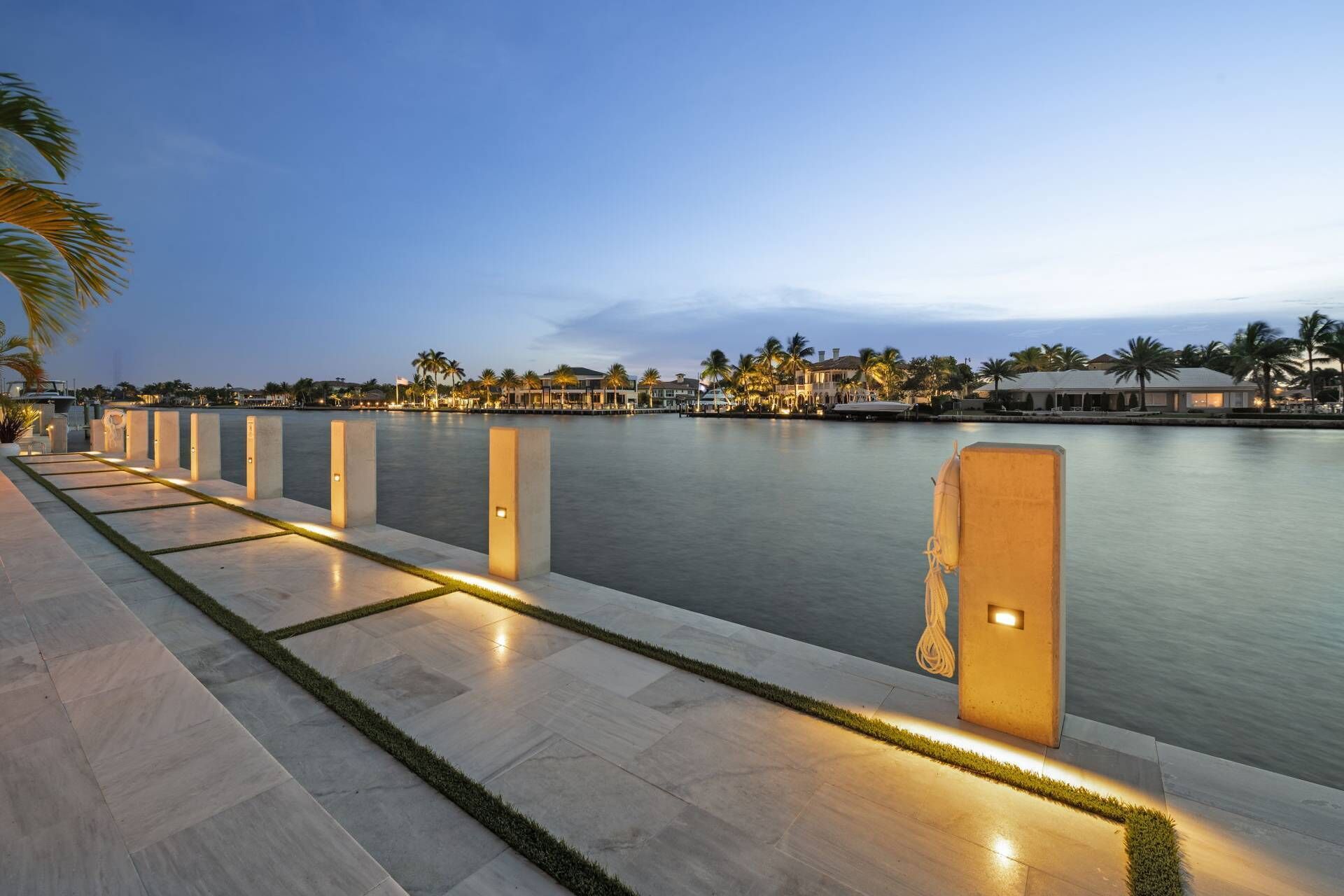 A waterfront promenade with a series of illuminated bollards and a calm body of water.