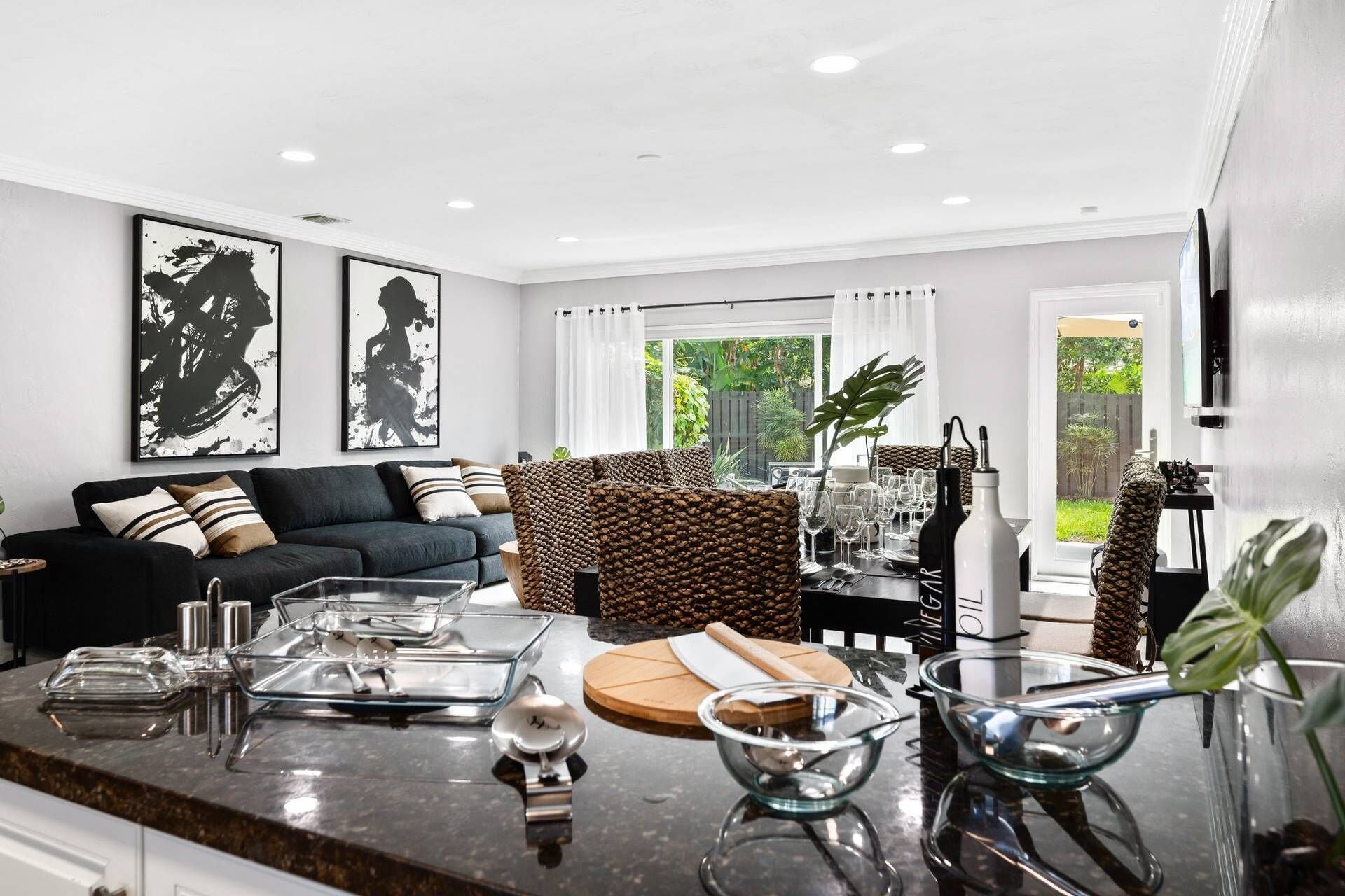 A modern living room with a dark sofa, a wicker chair, and a dining area with a glass table.