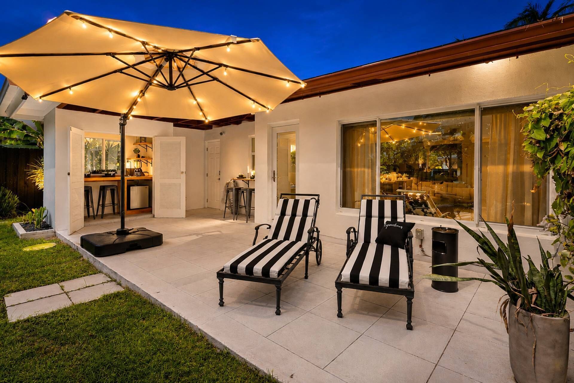 A patio with two lounge chairs, a large umbrella, and a dining area with a bar.