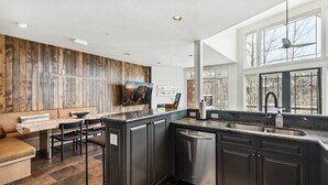 A modern kitchen with dark cabinetry, a central island, and a dining area with a sofa and table. - Ski-in/ski-out with private hot tub! Sleeps 12 (Telluride)