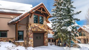 A snow-covered lodge with a stone facade, large windows, and a prominent chimney. - Ski-in/ski-out with private hot tub! Sleeps 12 (Telluride)