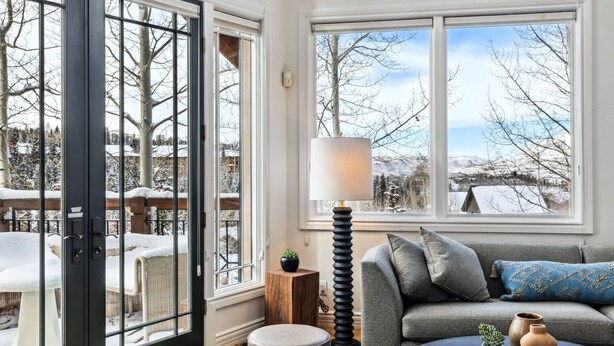 A cozy living room with a large window, a sofa, a lamp, and a view of a snowy landscape. - Ski-in/ski-out with private hot tub! Sleeps 12 (Telluride)