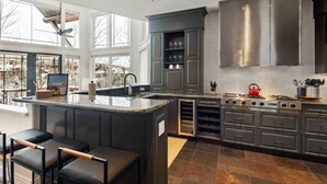 A modern kitchen with a central island, dark cabinetry, and a large window providing a view of a snowy landscape. - Ski-in/ski-out with private hot tub! Sleeps 12 (Telluride)