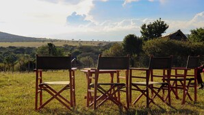 Un campo cubierto de césped con tres sillas de director de madera y una mesa de madera.