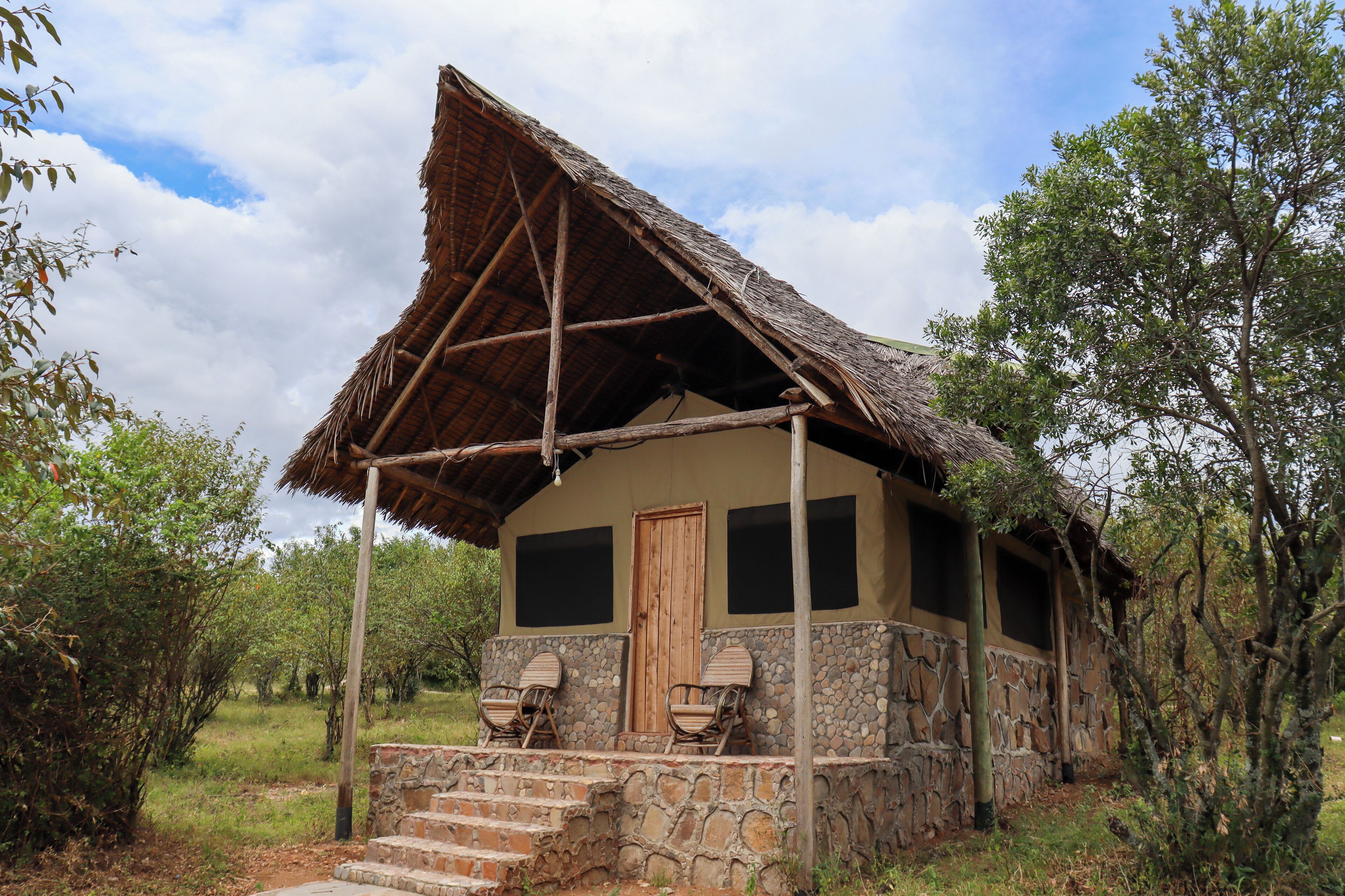 A rustic building with a thatched roof, stone walls, and a porch with two chairs.