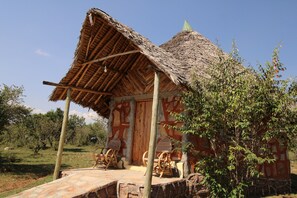 A rustic hut with a thatched roof and a wooden door, surrounded by greenery and a stone pathway. - Orngatuny Mara King Camp (Maasai Mara)