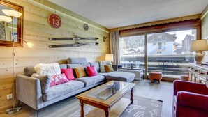 Un salón moderno con un sofá seccional gris, una mesa de centro de vidrio y una pared de madera con equipo de esquí.