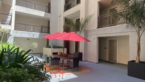 A multi-level atrium with a dining area featuring a table, chairs, and a red umbrella.