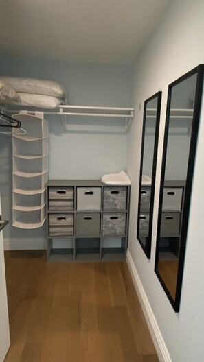 Een kleine, smalle kamer met een houten vloer, een witte kast met kledingroede en twee grote spiegels aan de rechterwand.