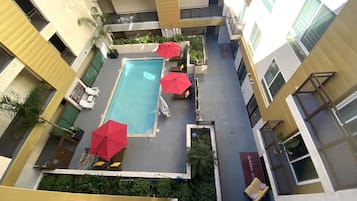 Luchtbeeld van een hotel binnenplaats met een zwembad, meerdere rode parasols en ligstoelen.