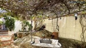 Une terrasse dallée de pierres, avec un banc en pierre, une petite fontaine et une pergola couverte de plantes grimpantes.