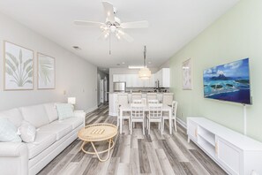 A modern living room with a sofa, dining table, and chairs, a ceiling fan, and artwork on the walls.