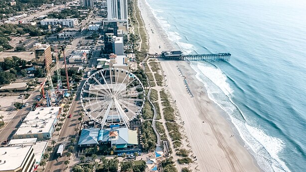 An aerial view of a coastal area with a large Ferris wheel, beachfront, and a pier. - Golf Course Condo with Resort Style Pool, 5 Miles from Beach, Fully updated (Myrtle Beach)